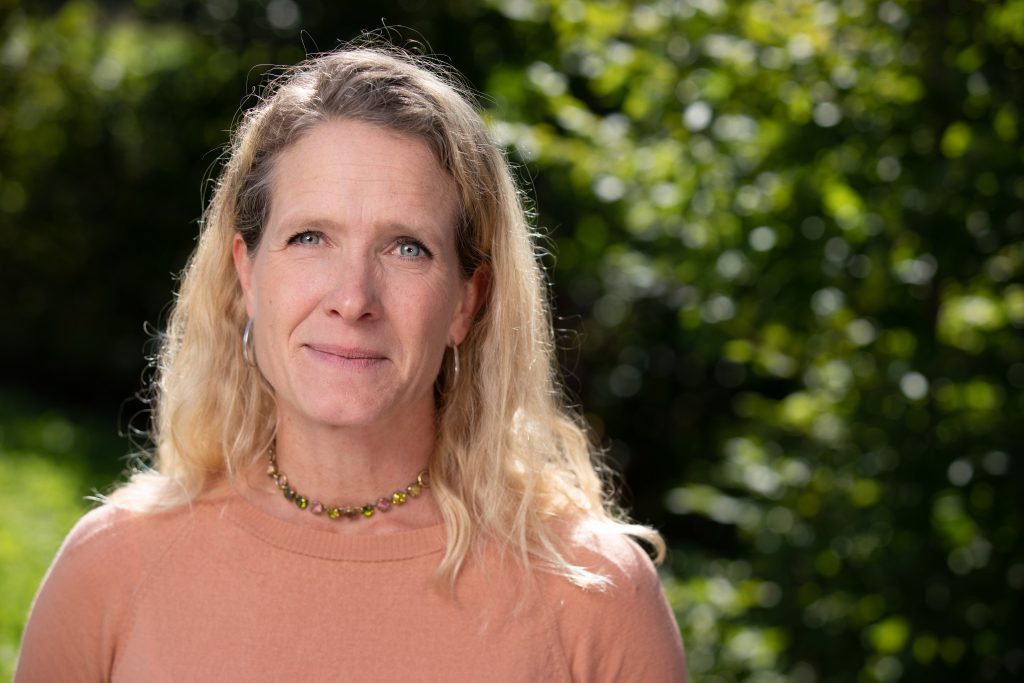 Lena Staafgard, COO of Better Cotton, wearing a peach-coloured top posing in front of green trees on a sunny day.